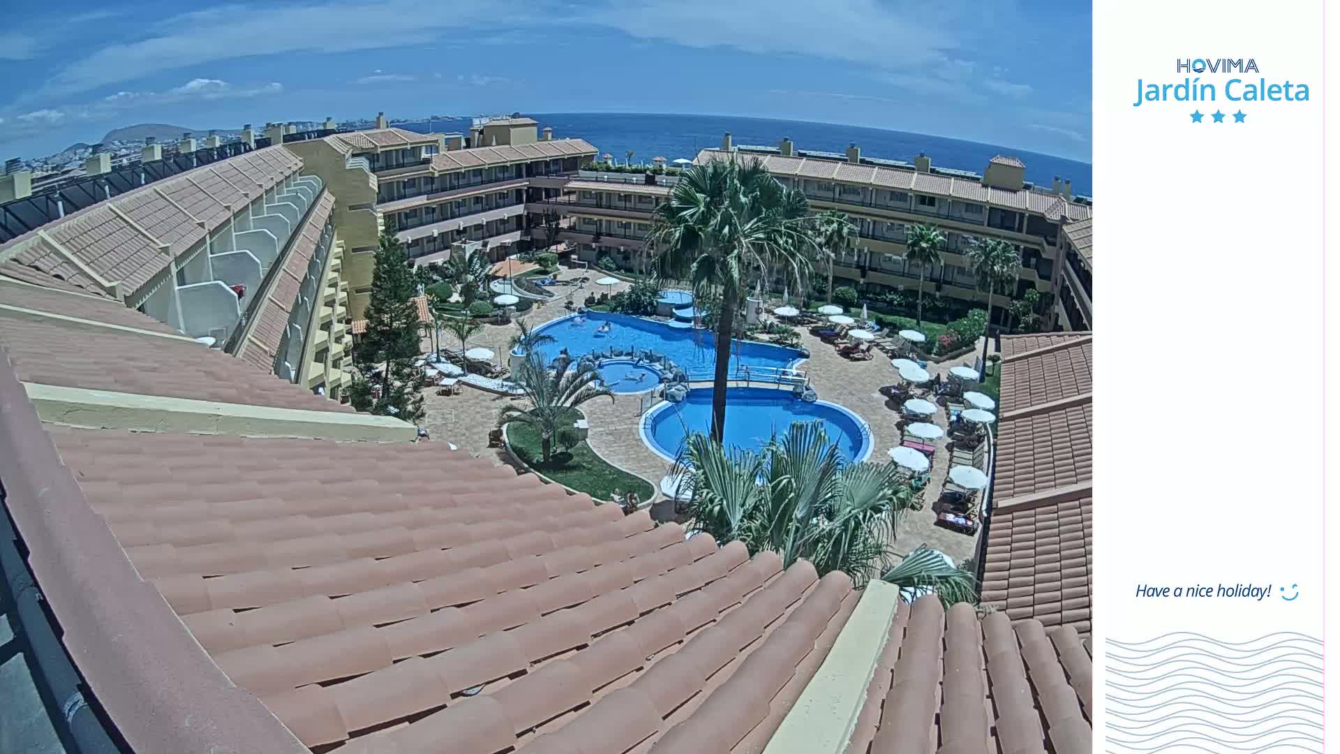 A tiled roof overlooks a resort pool area with multiple pools, palm trees, and lounge chairs under sunny skies.