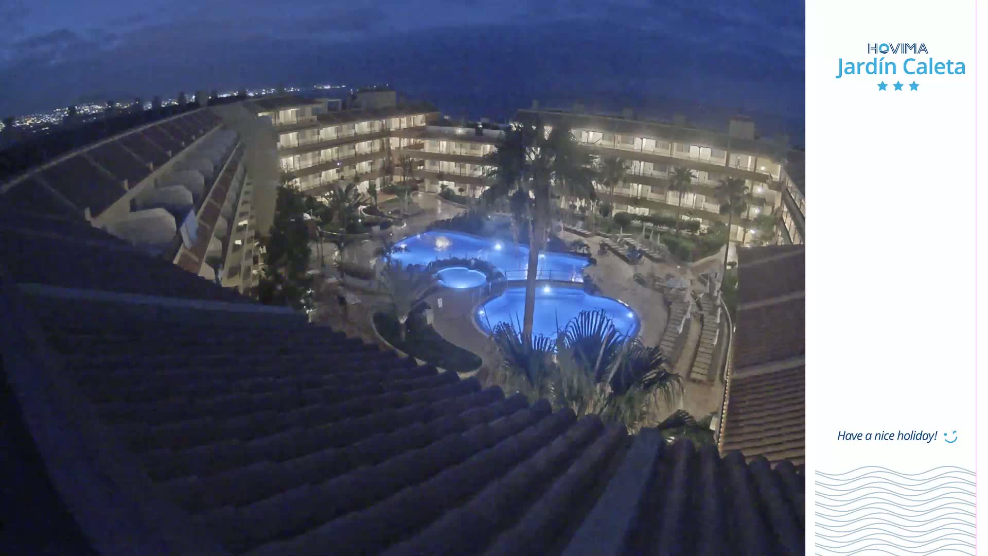 An illuminated apartment complex with a swimming pool is viewed from above at night.