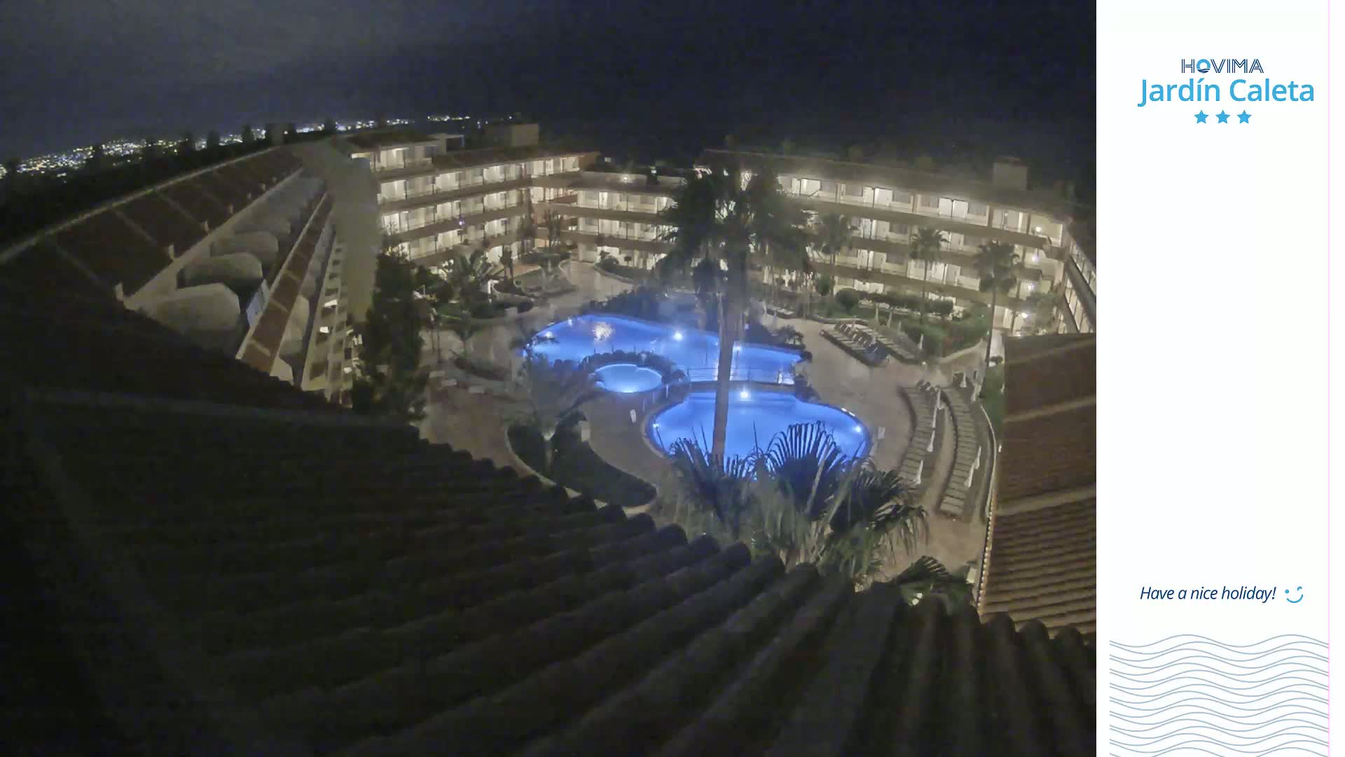 A nighttime aerial view shows a multi-story hotel complex surrounding a lit pool area.