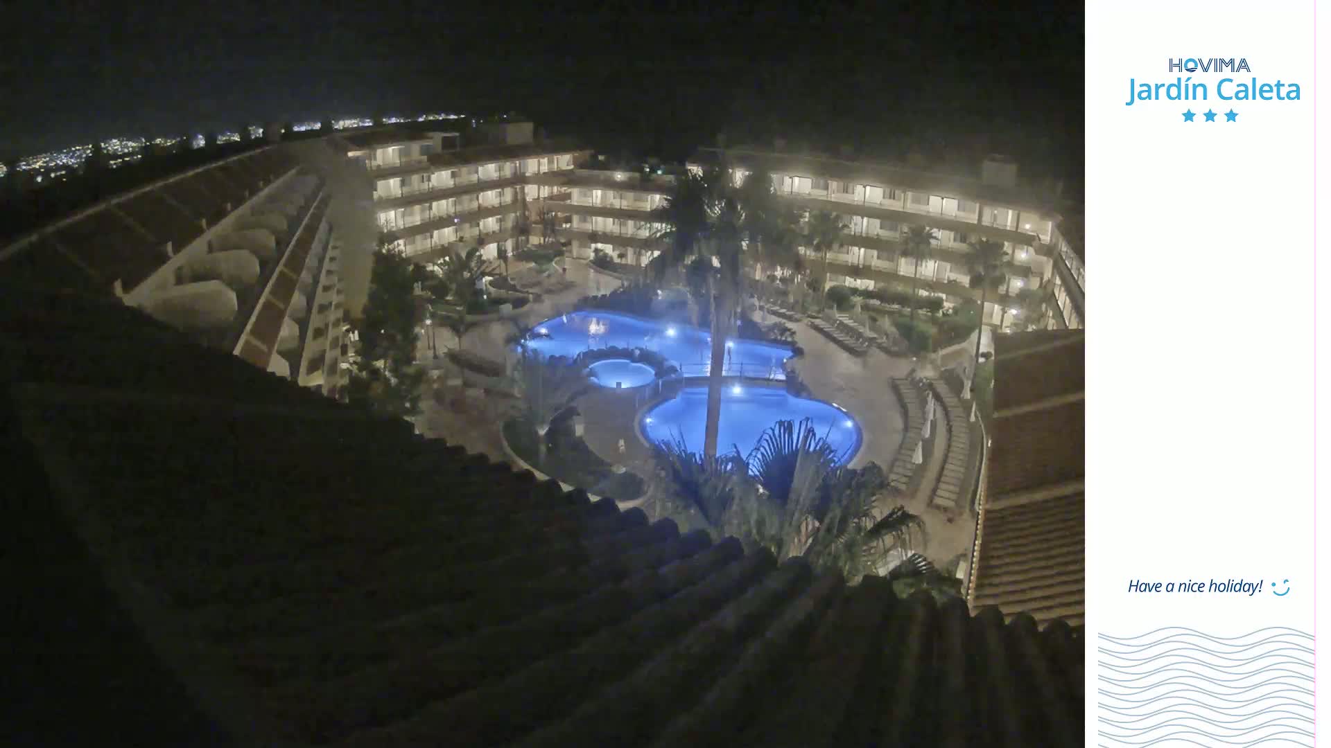 A nighttime, overhead view shows a multi-story building complex surrounding a lit swimming pool area.