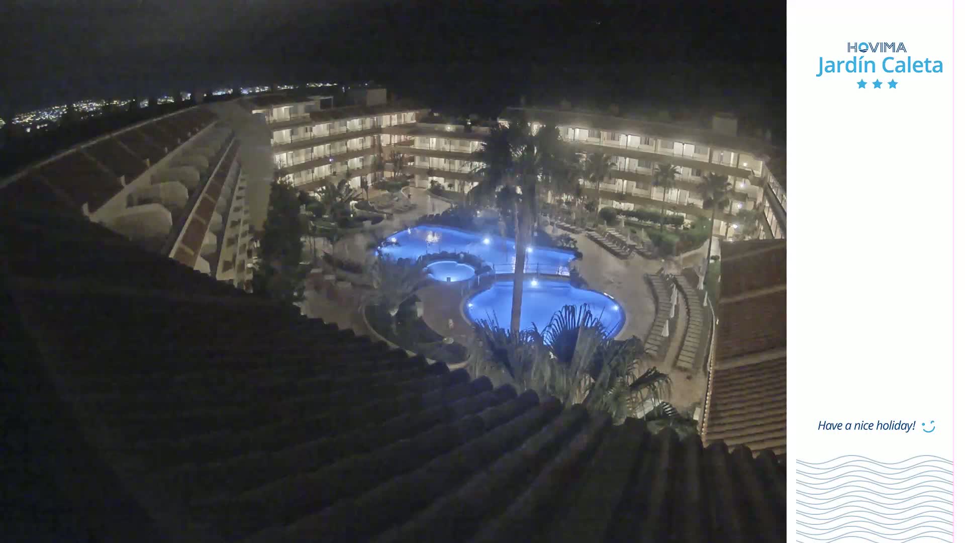 A nighttime, overhead view of a multi-story resort complex with multiple illuminated swimming pools surrounded by landscaping.