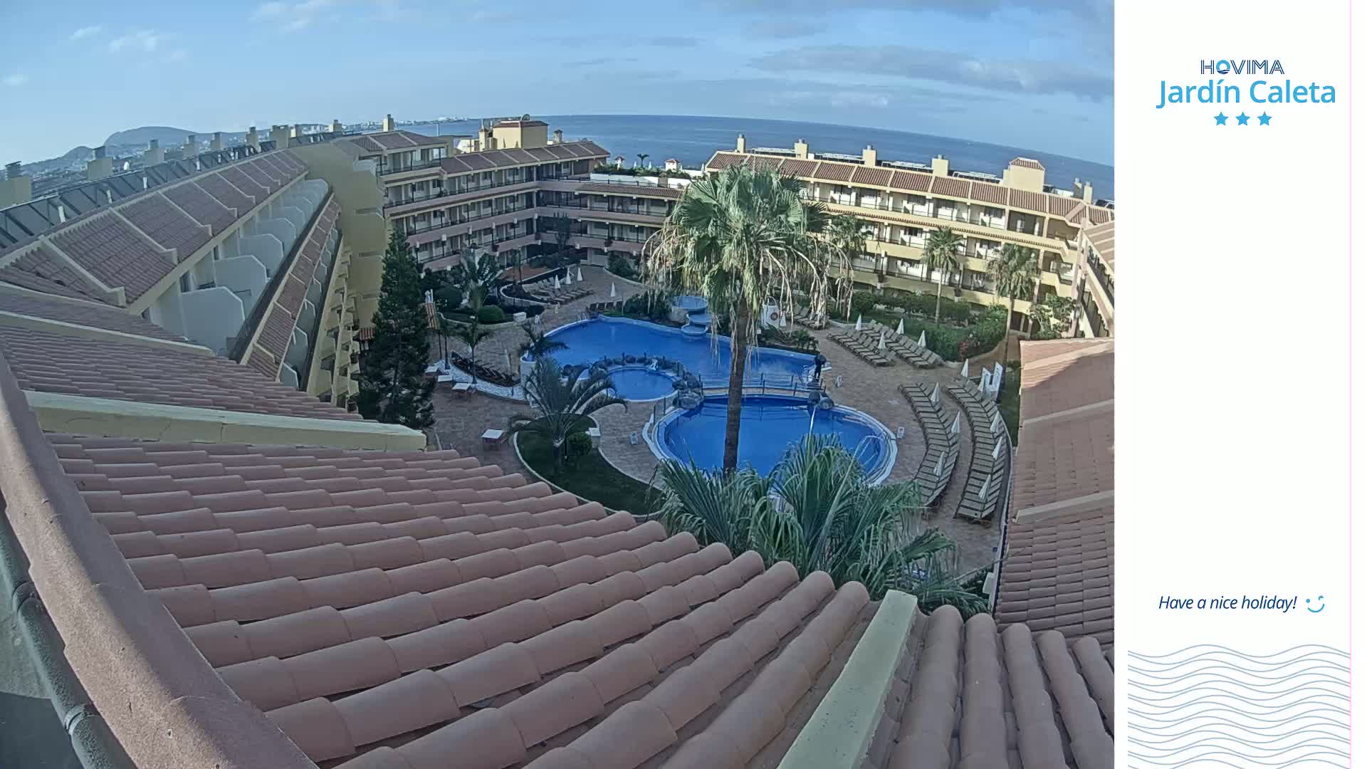 A tiled roof overlooks a resort pool area with surrounding buildings, under a clear sky.