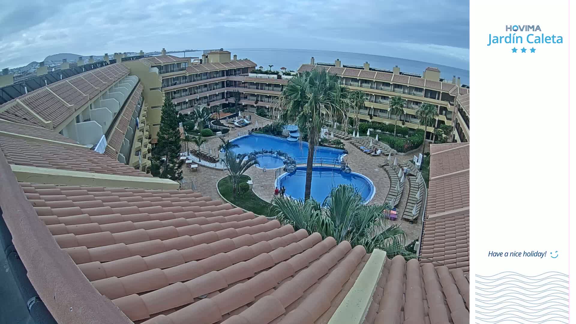 An overhead view shows a multi-story building complex surrounding a swimming pool on an overcast day.