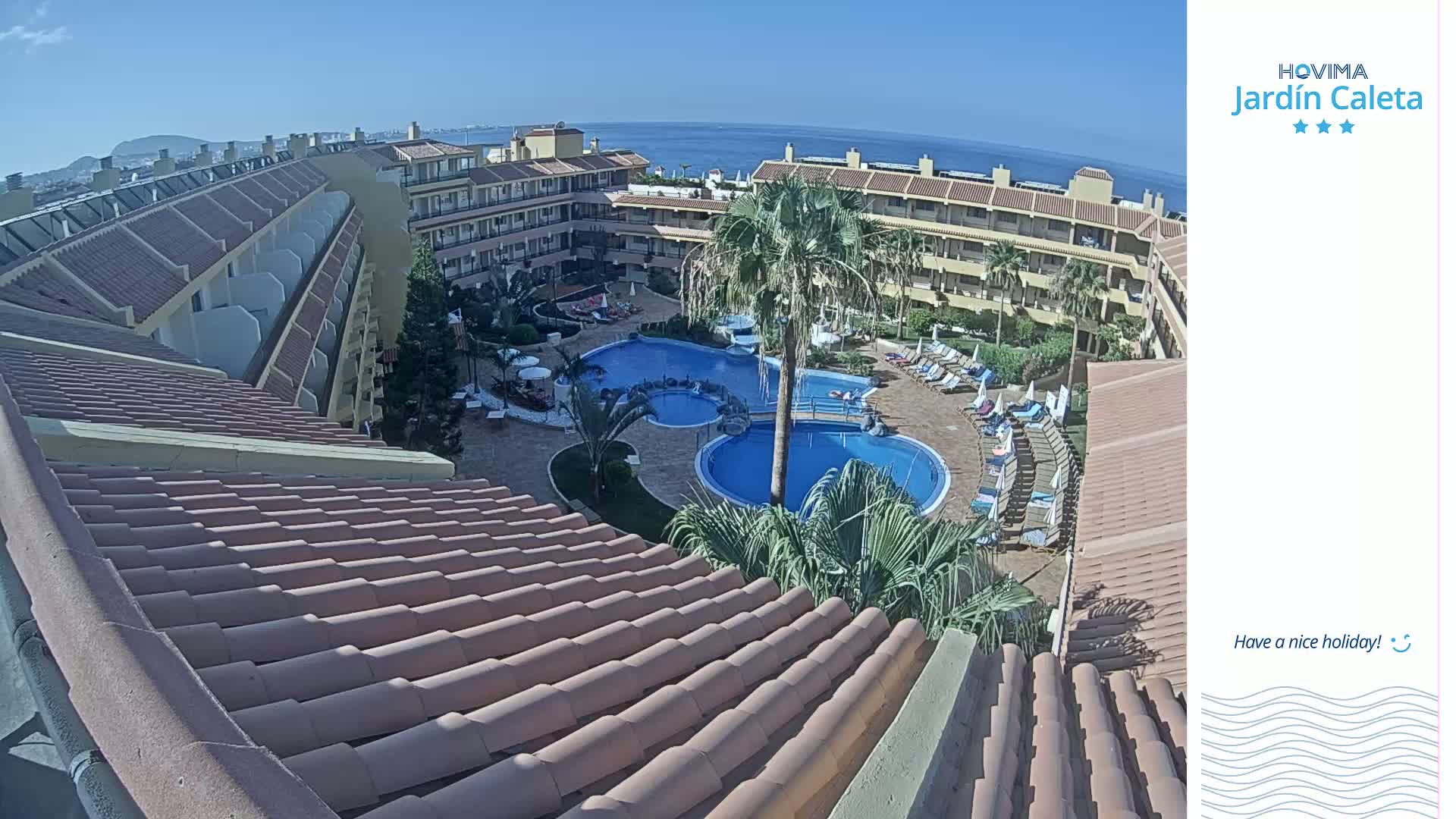 A sunny view overlooks a resort's pool area and surrounding buildings from a tiled roof.