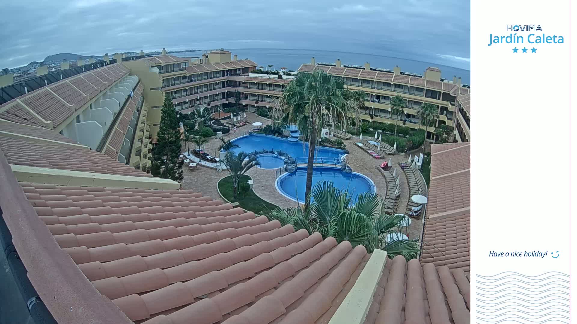 An overhead view of a resort complex with a swimming pool and surrounding buildings on an overcast day.
