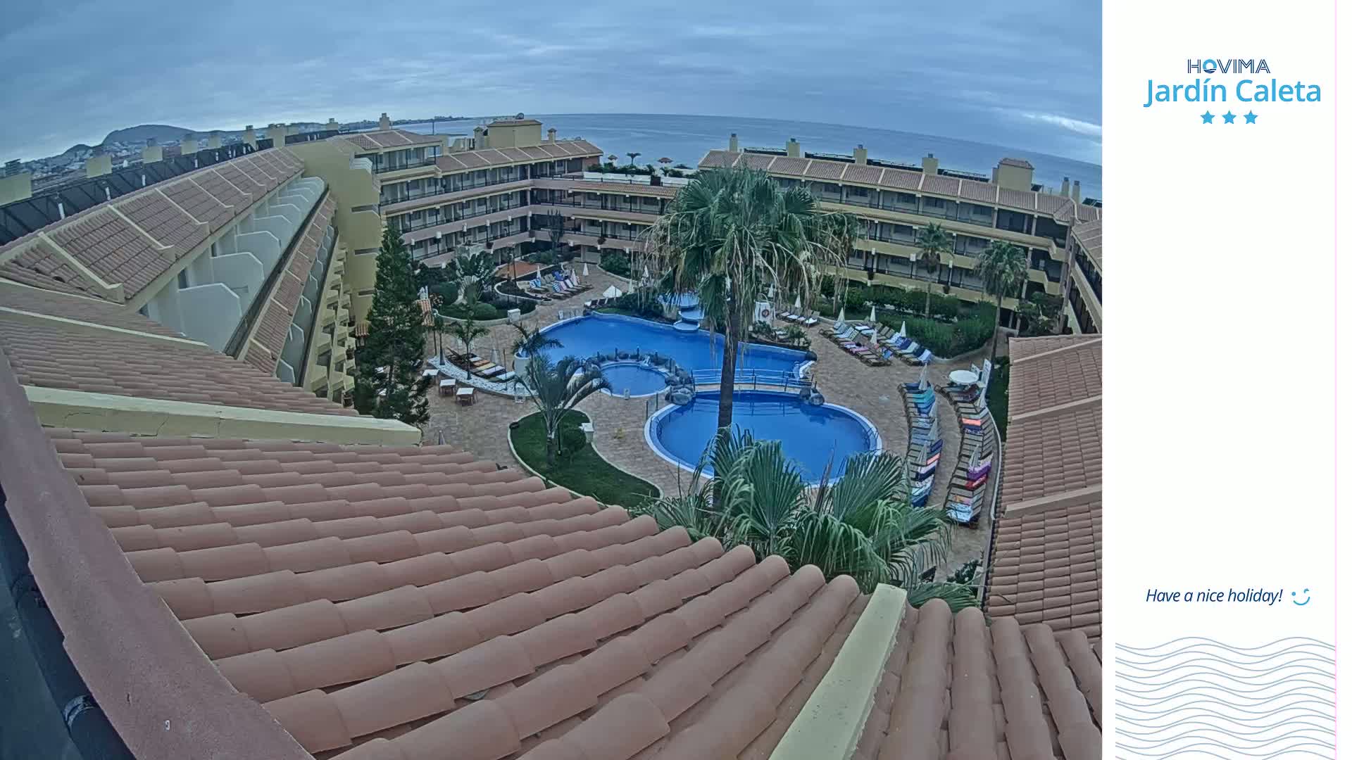 An overhead view of a resort pool area with surrounding buildings under an overcast sky.
