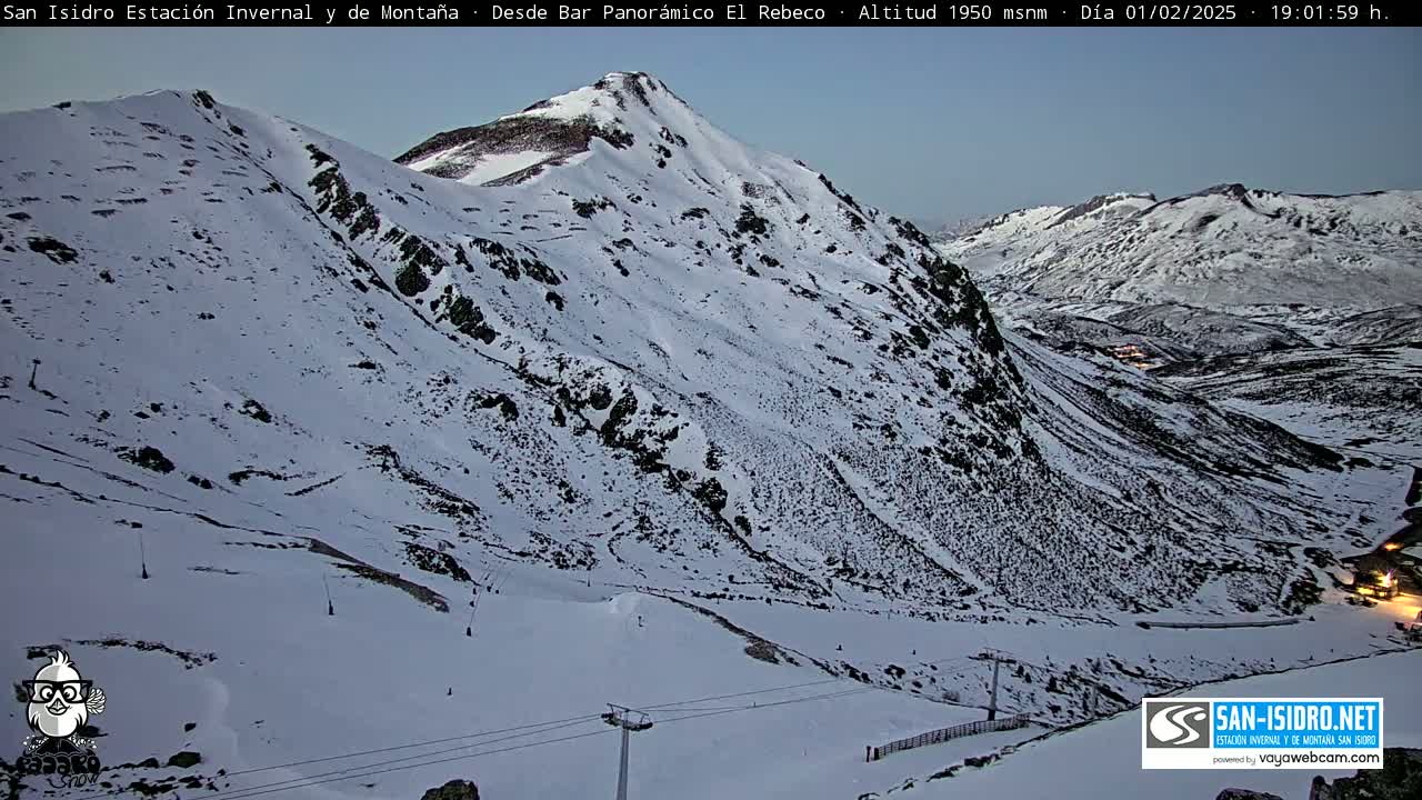 A snow-covered mountain slope at dusk, with ski lift infrastructure visible.
