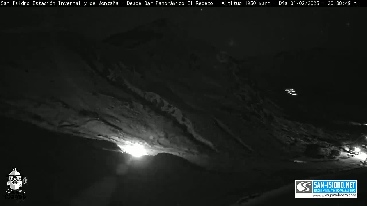 A nighttime, snow-covered mountain slope is illuminated by artificial lights from a distance.