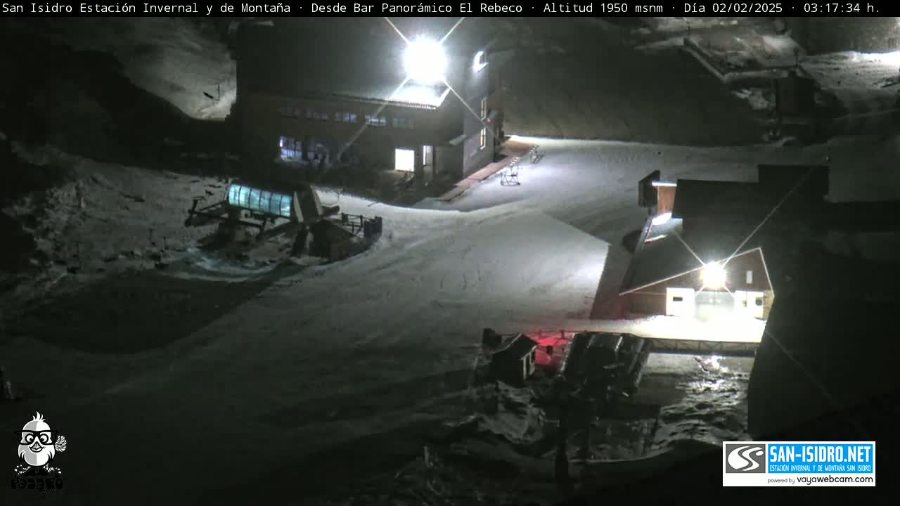 A snow-covered ski resort at night, illuminated by artificial lights.