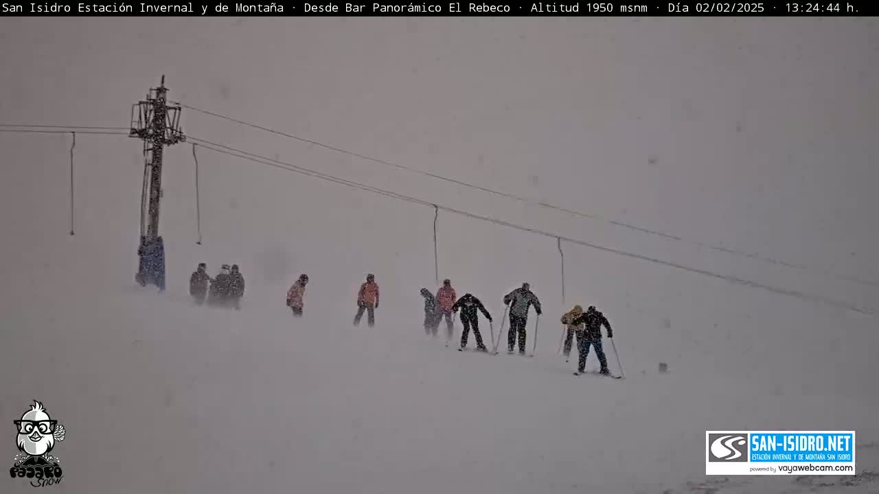 A snow-covered ski slope with several skiers and a ski lift in heavy snowfall.
