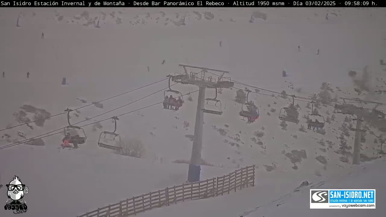 A snowy mountain slope with a chairlift and several skiers visible through blowing snow.