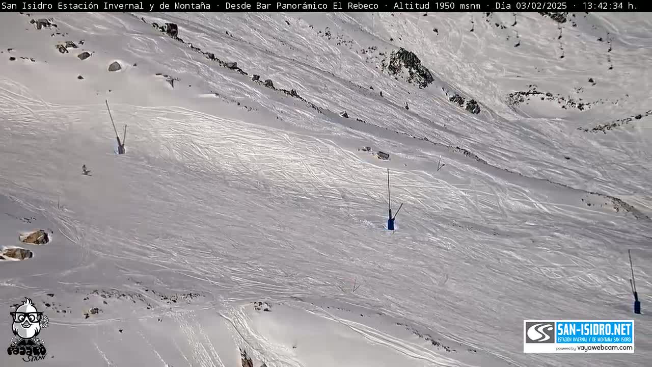 A snow-covered ski slope with several ski lift poles and visible ski tracks under bright, sunny conditions.