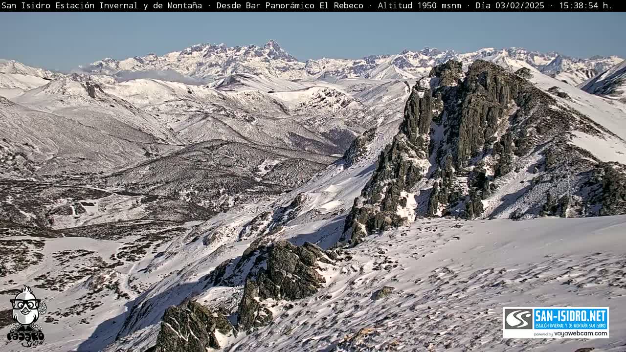 A snow-covered mountainous landscape is viewed from a high vantage point on a sunny day.