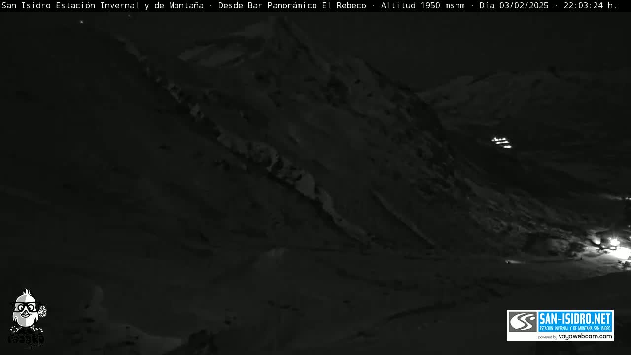 A nighttime, low-light view of a snow-covered mountain slope with a few distant lights visible.
