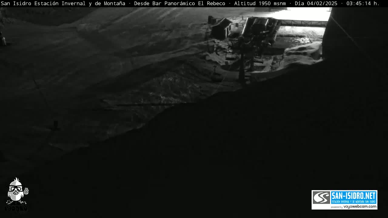 A nighttime, low-light view of a snow-covered mountain slope with a structure at the top.