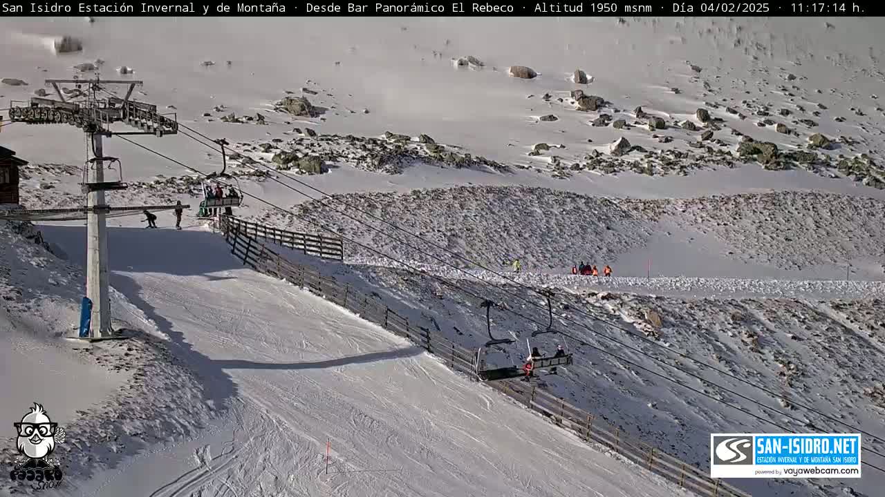 A ski slope with a chairlift and several skiers and snowboarders on a mostly sunny day with patches of snow.