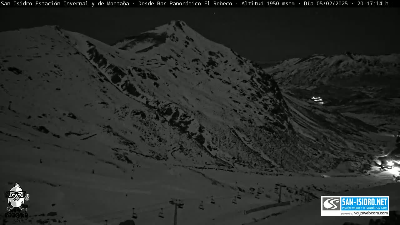 A snow-covered mountainside is visible at night, with some lights in the distance.