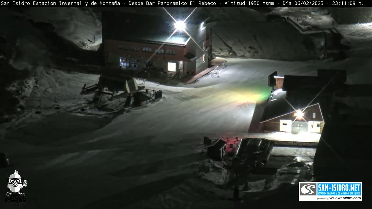 A snow-covered ski resort at night is illuminated by artificial lights.