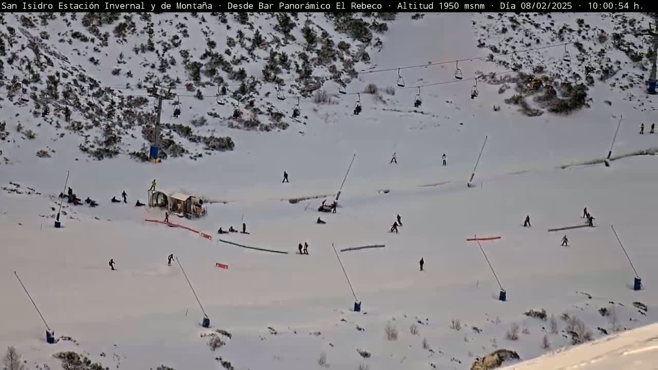 A snowy ski slope with several skiers and snowboarders, a chairlift, and some machinery.