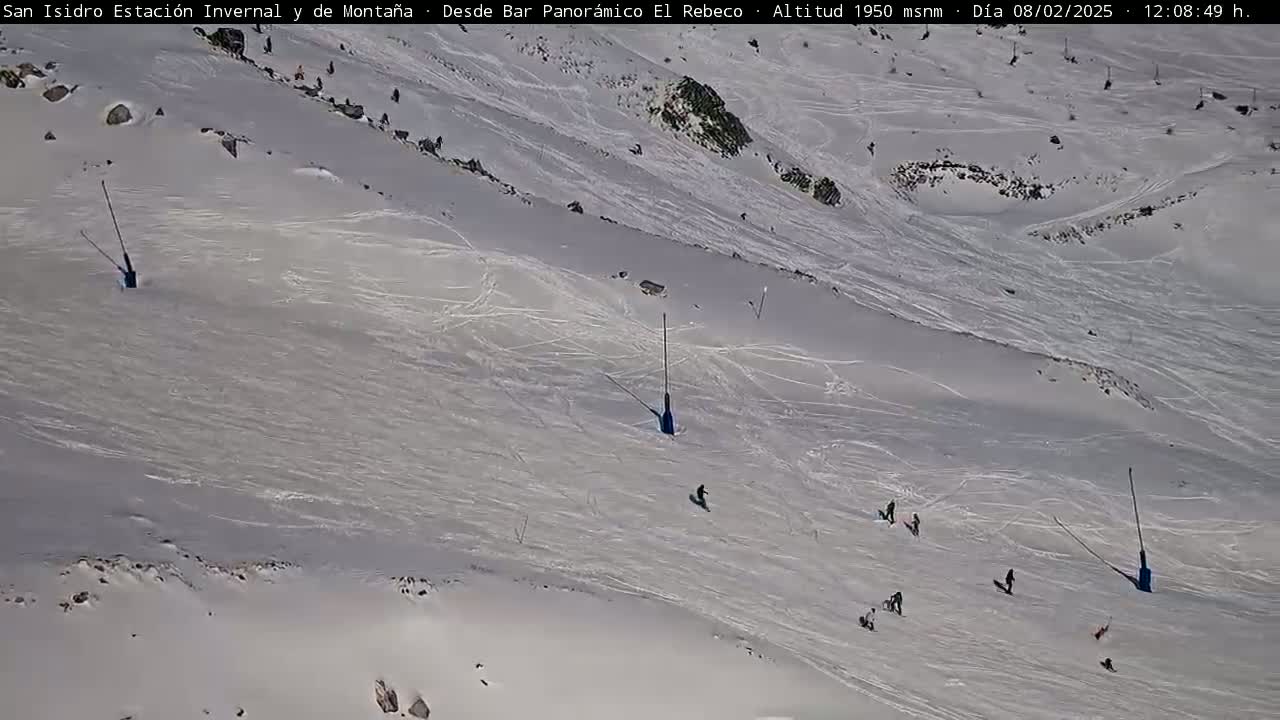 A snowy, sunny ski slope with several skiers and snowboarders.