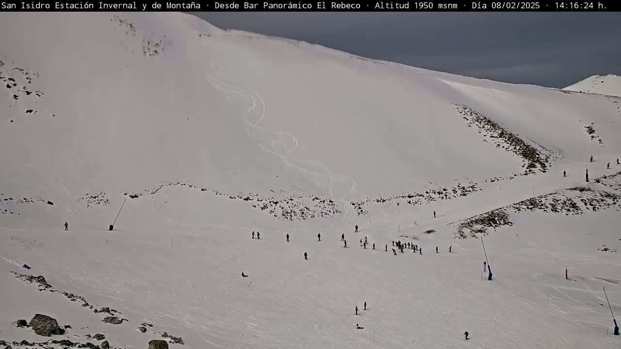 A snowy mountain slope with several skiers and snowboarders scattered across it under an overcast sky.