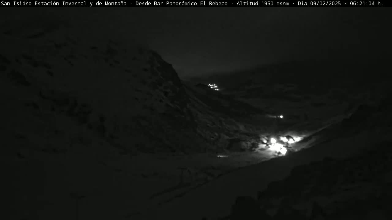 A nighttime, snow-covered mountain slope is illuminated by several distant lights.