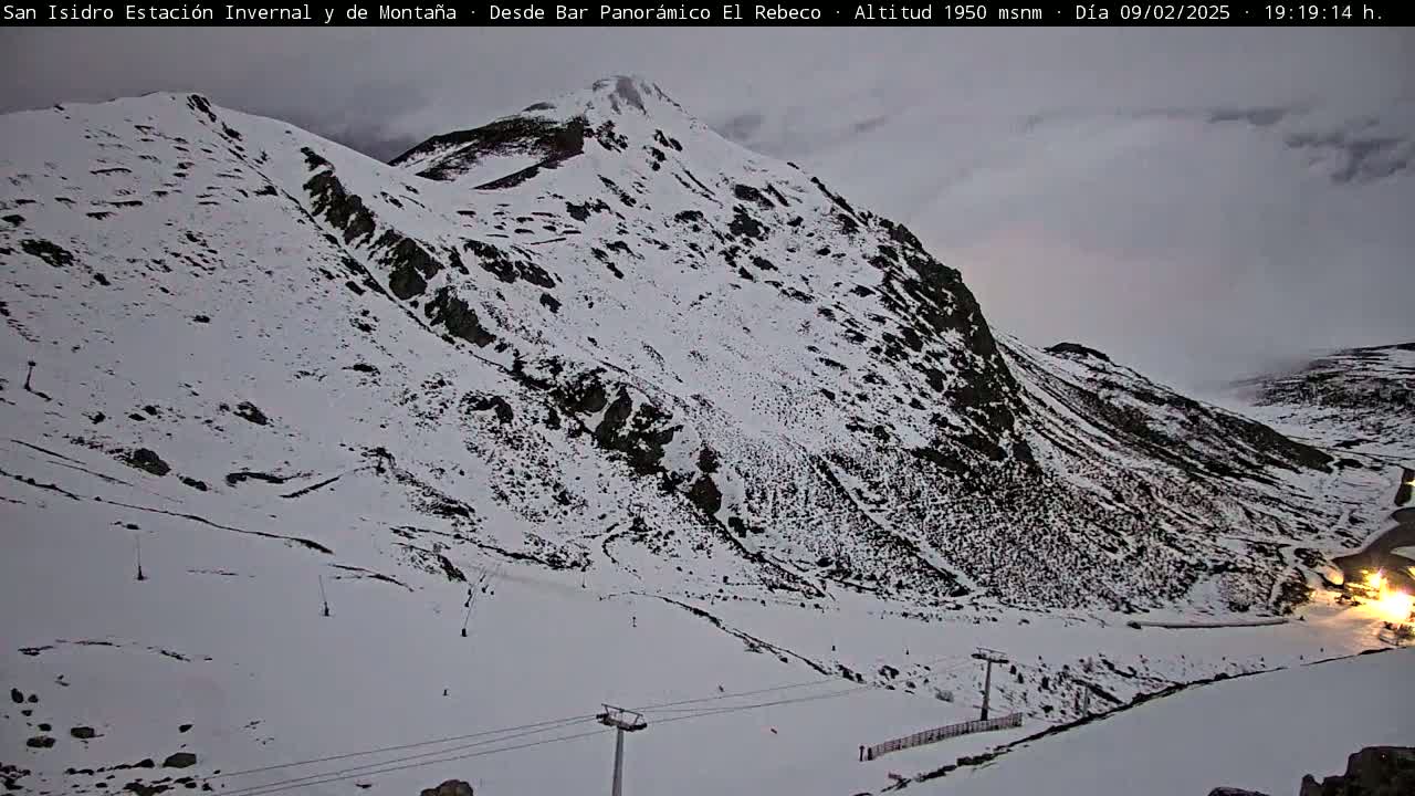 A snow-covered mountain slope with ski lifts under an overcast sky.