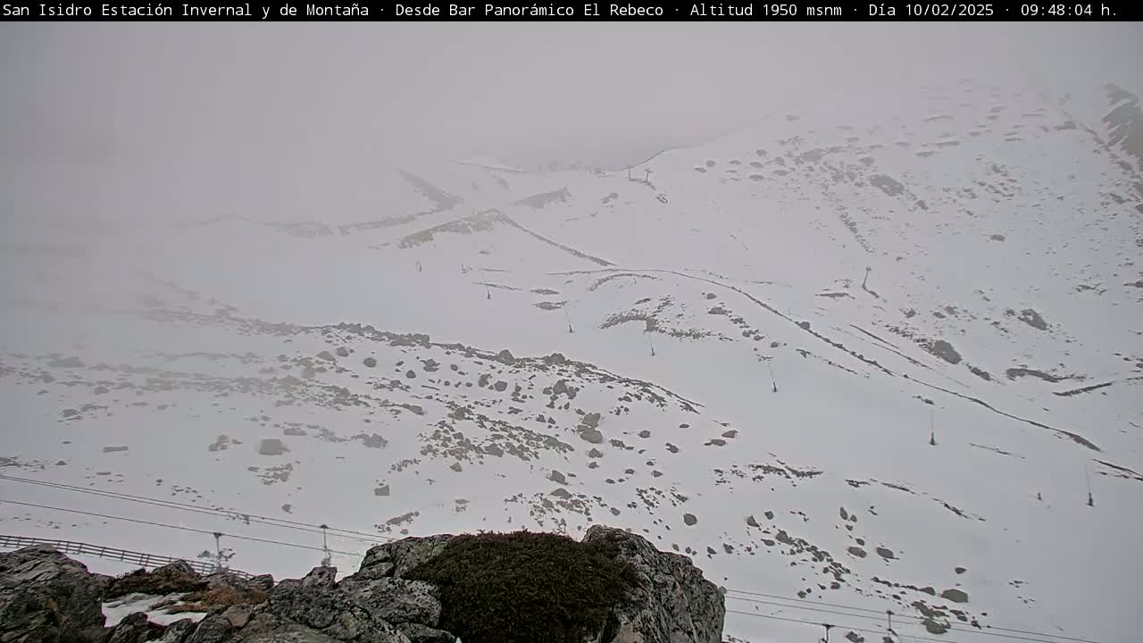 A snowy, foggy mountain landscape is visible from a rocky outcrop, with ski lift infrastructure in the distance.