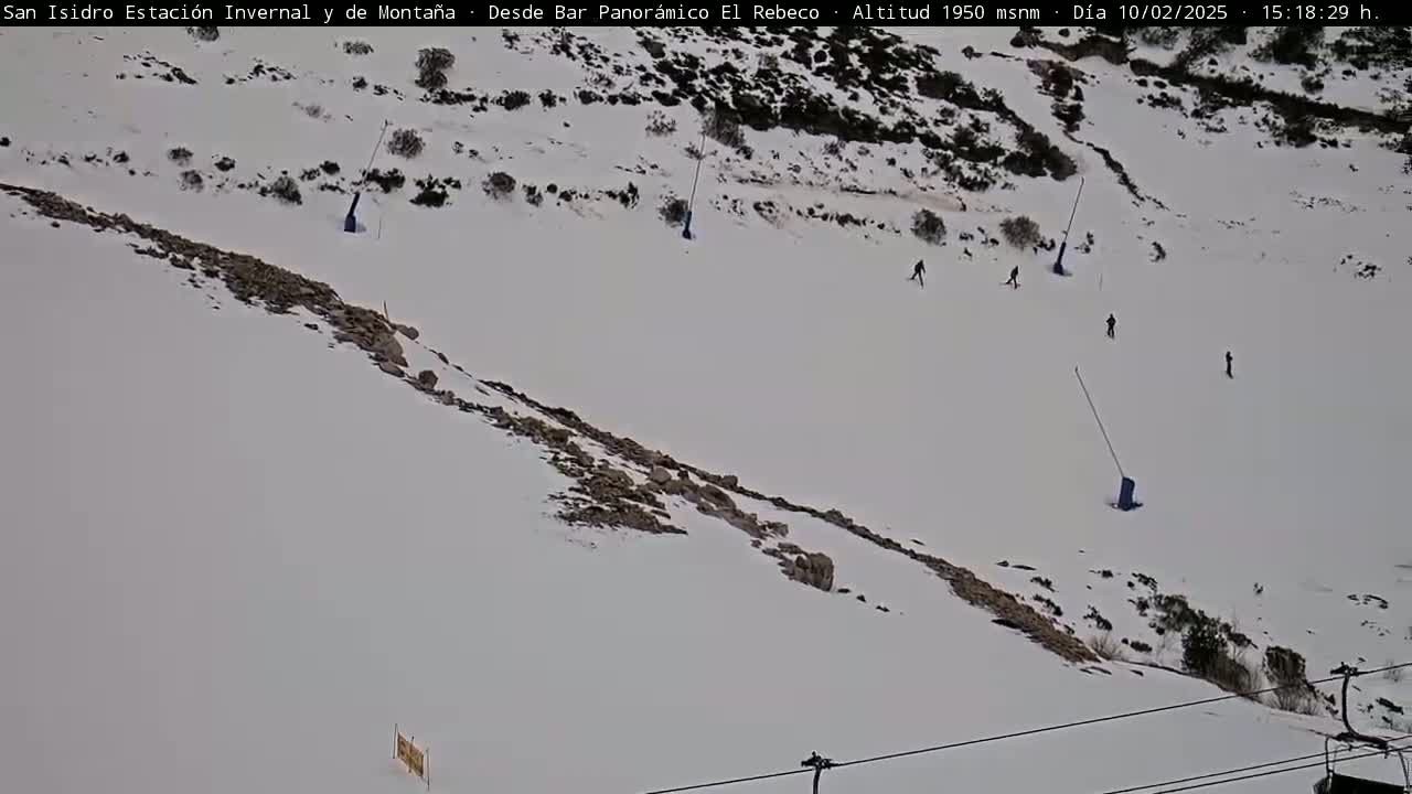 A snowy mountain slope with several skiers and ski lifts.