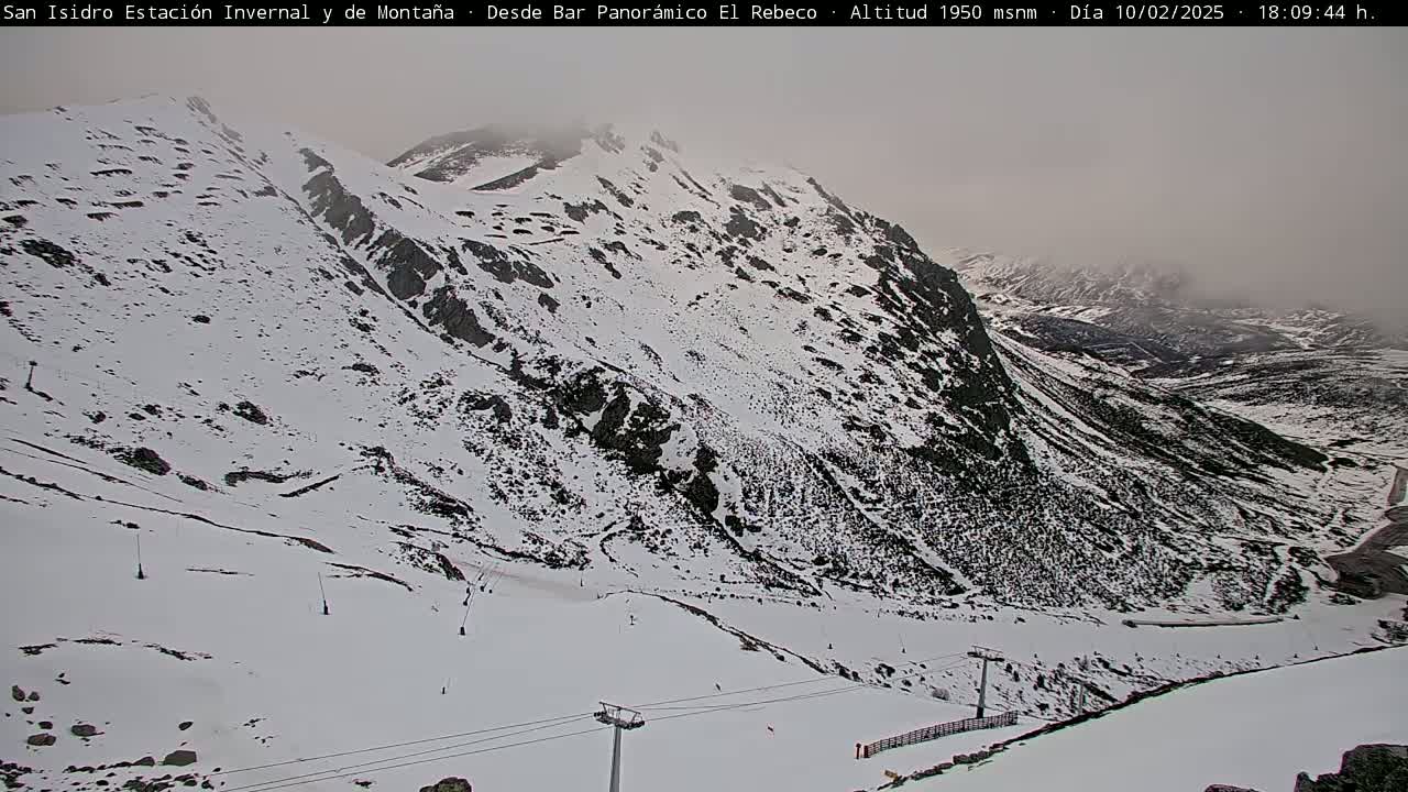 A snow-covered mountain slope with ski lifts and a foggy sky.