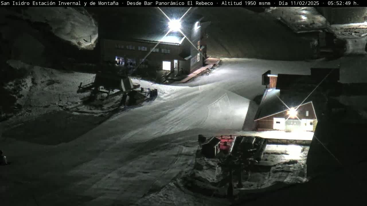 A nighttime view of a snow-covered ski resort with buildings illuminated by lights.