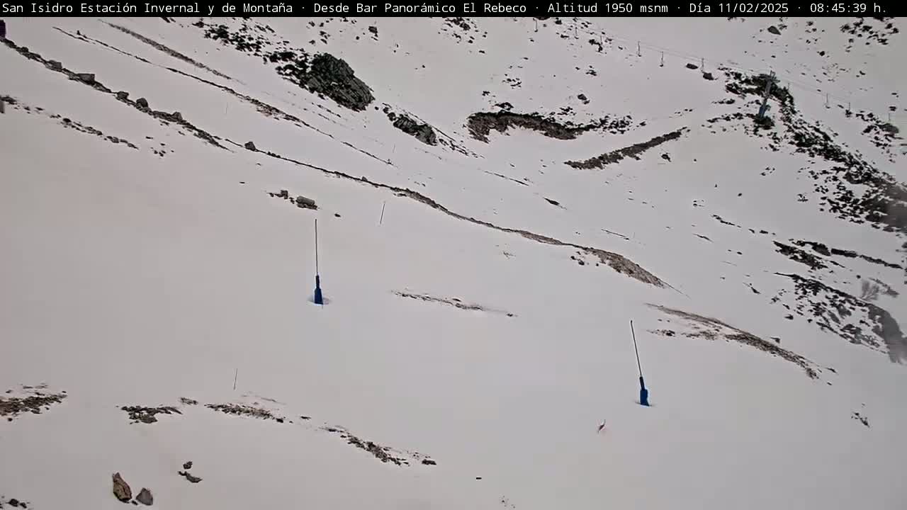A snow-covered mountain slope with two blue markers and some exposed rocks under a cloudy sky.