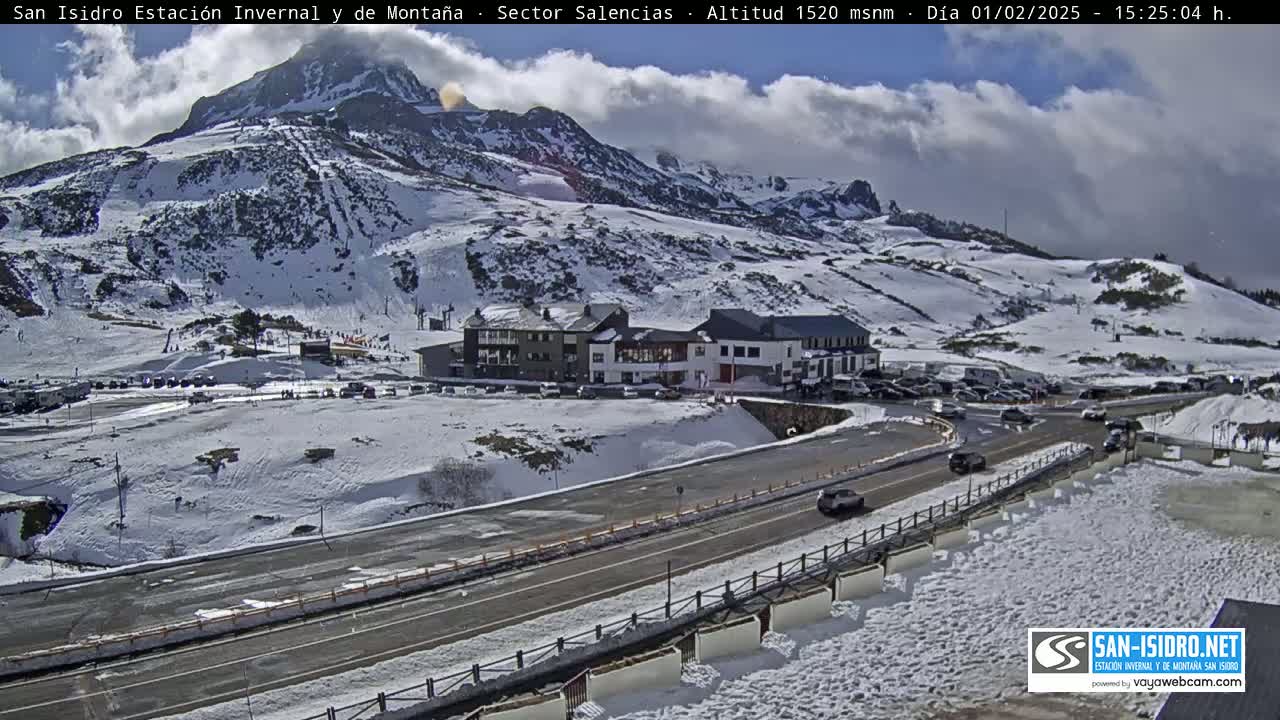 A snow-covered mountain resort with a road and several buildings is visible under a partly cloudy sky.