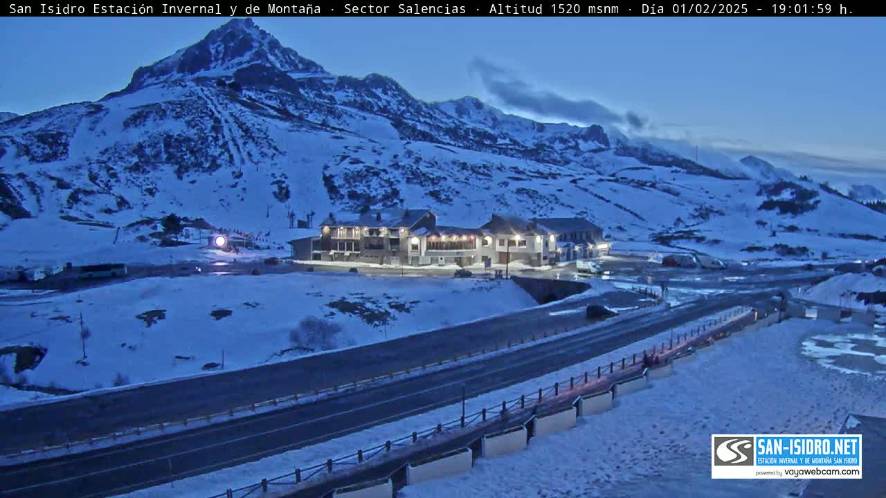A snow-covered mountainside with a building complex and a road below, under a twilight sky.