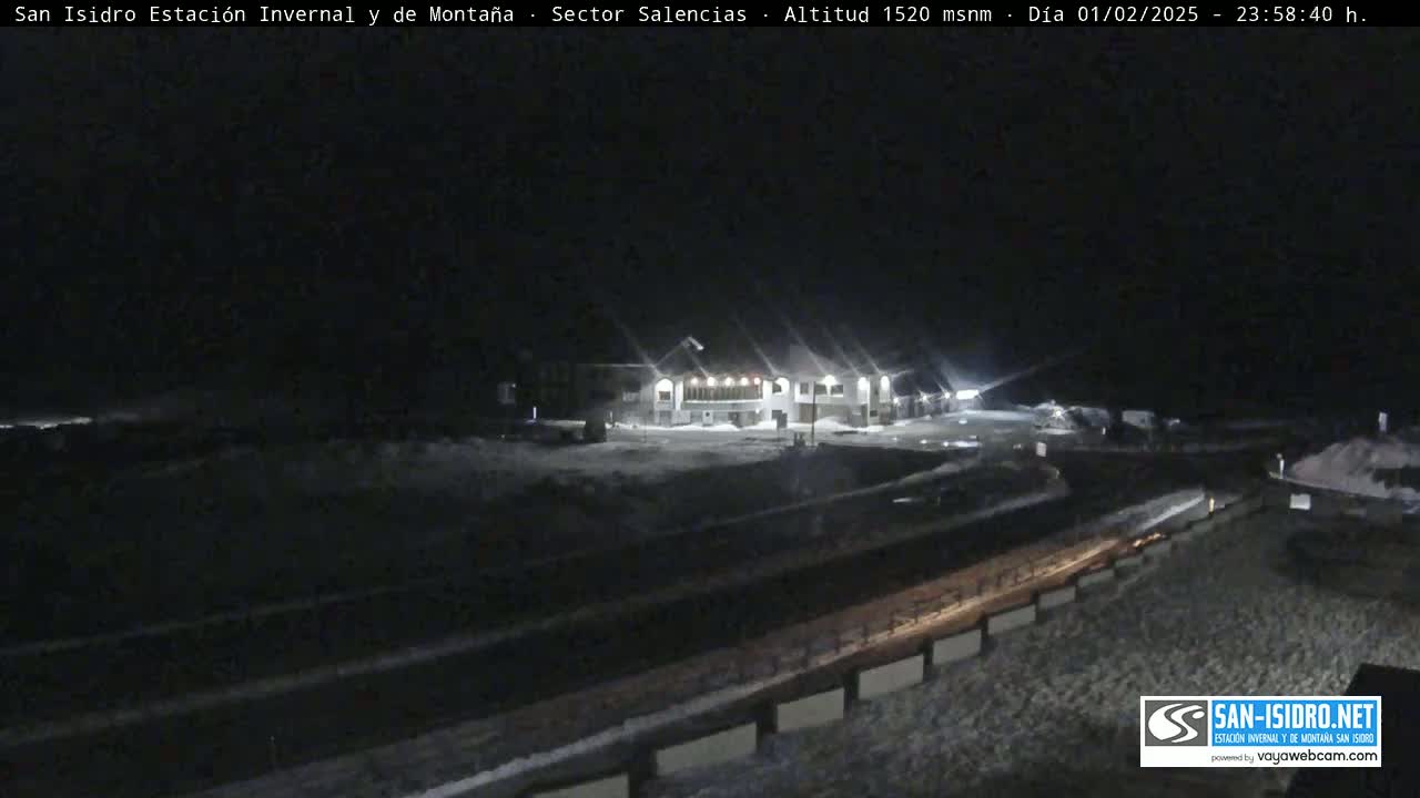 A nighttime, snow-covered scene shows a lit building near a road, with a dark sky.