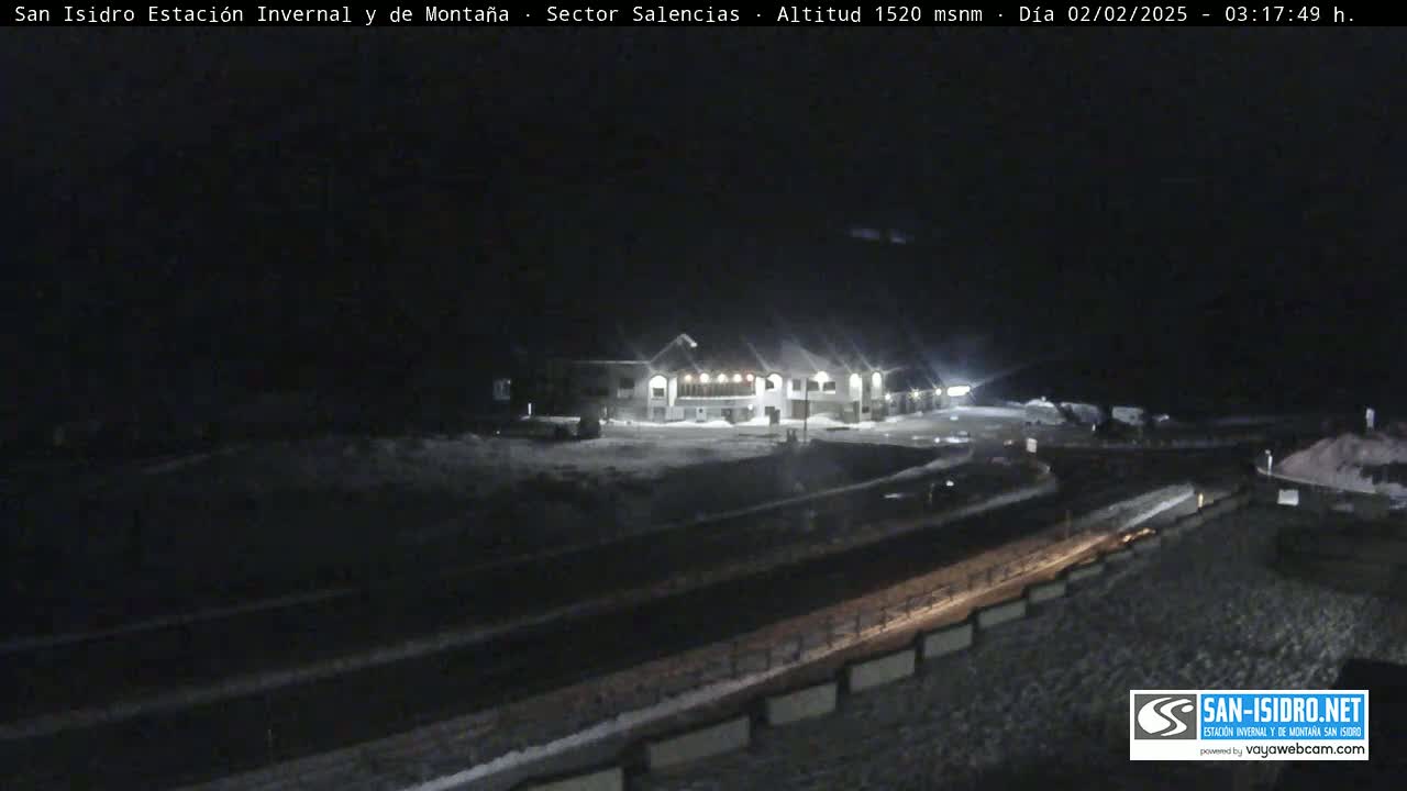 A snow-covered building complex is illuminated at night, with a road and surrounding areas also covered in snow.