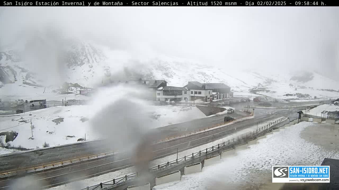 A snow-covered mountain landscape with a building complex and road, viewed through a snow-obscured lens in foggy conditions.
