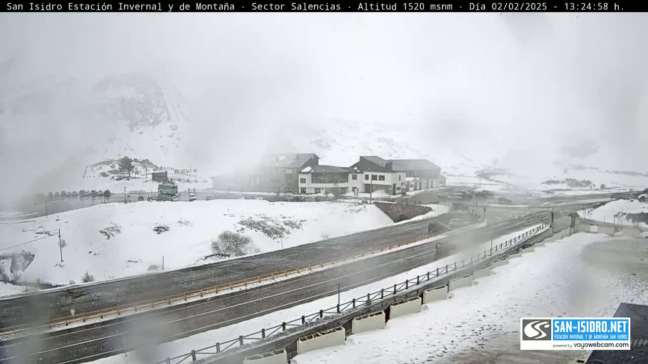 A snow-covered mountain landscape with a road and a building, under a foggy, snowy sky.