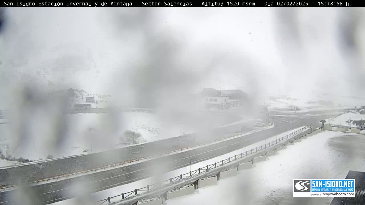 A snow-covered landscape with a road and buildings is visible through heavy snowfall.