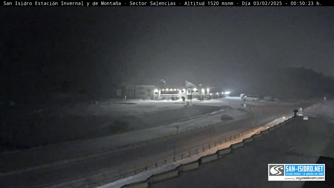 A snow-covered landscape at night shows a large building near a road.