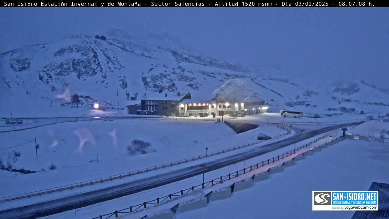 A snow-covered mountainside with a building and road, under a twilight sky.