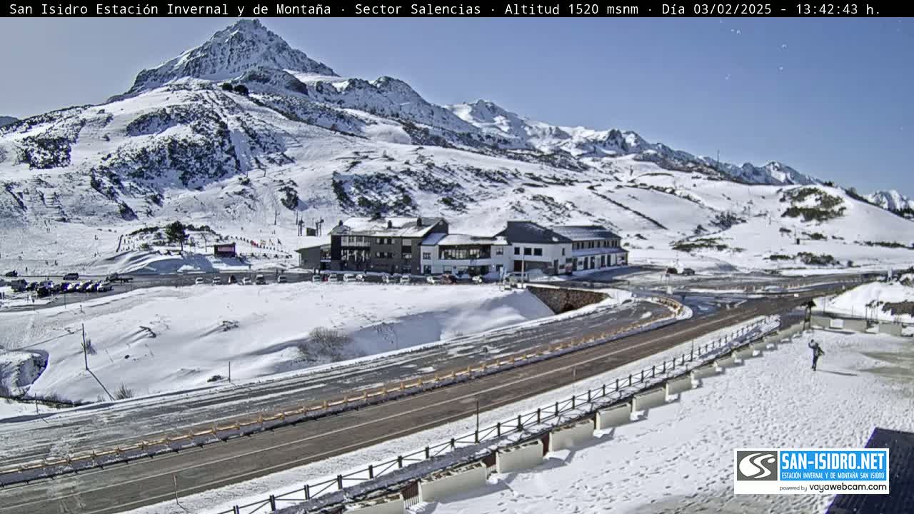 A snow-covered mountainside with a building complex and road, under a sunny sky.