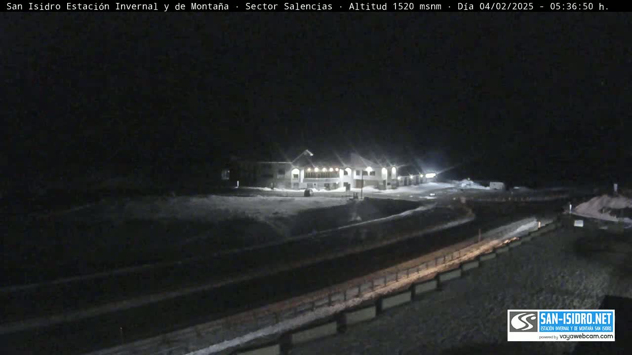 A snow-covered building complex is illuminated at night, with a road and snow-covered areas visible in the foreground.