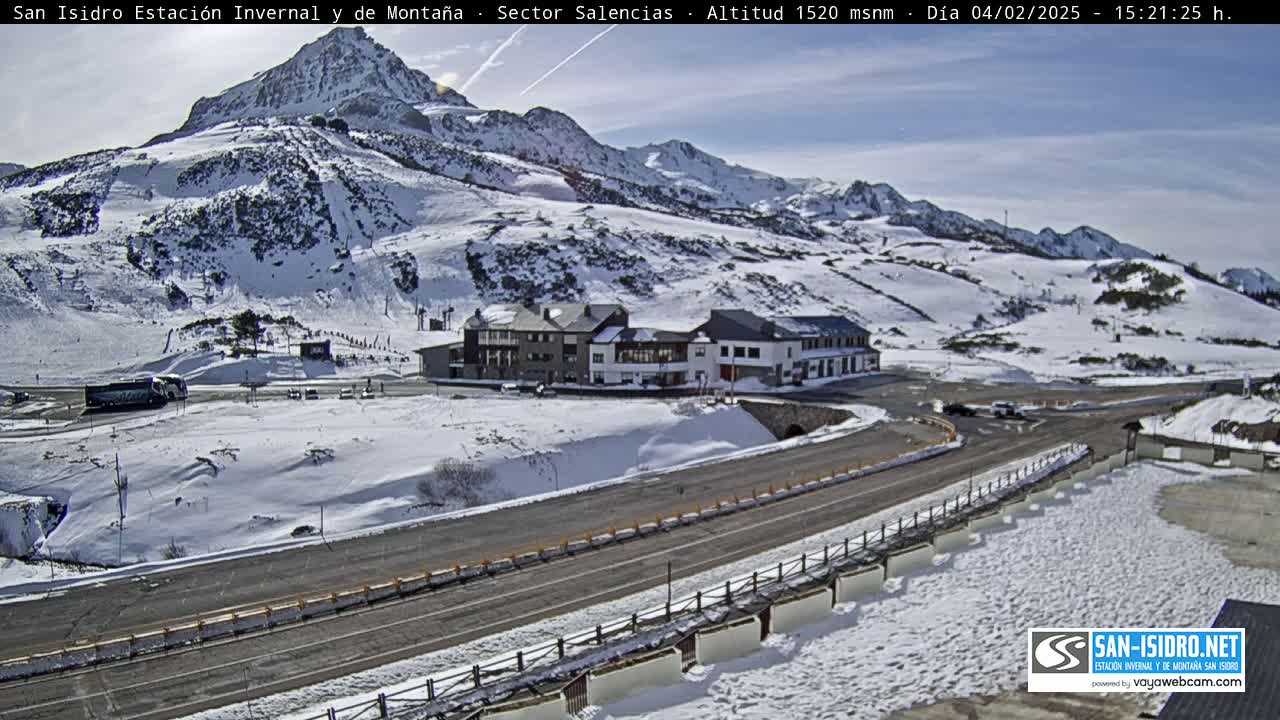 A snow-covered mountain landscape with a road and buildings, under a sunny sky.