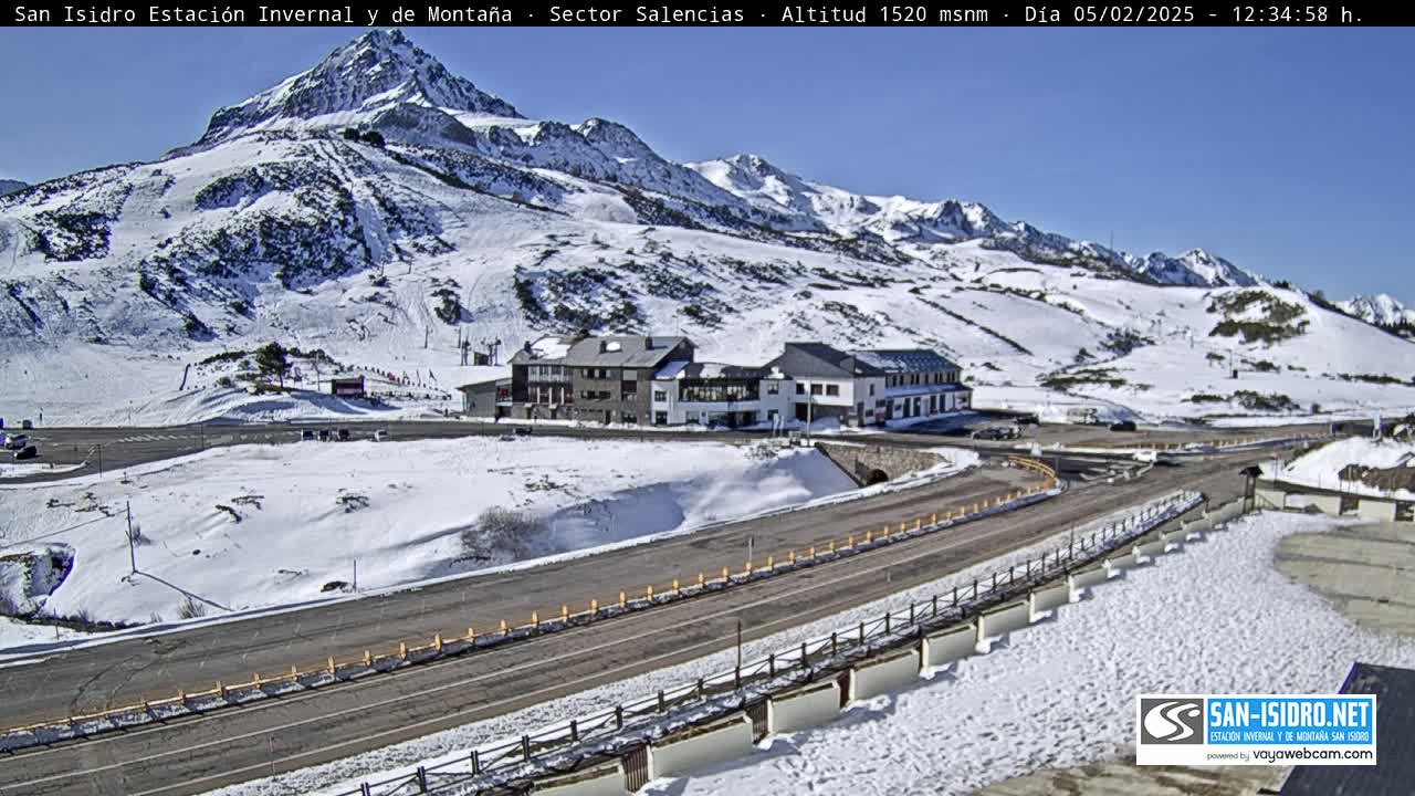 A snow-covered mountainside with a road and buildings, under a clear blue sky.