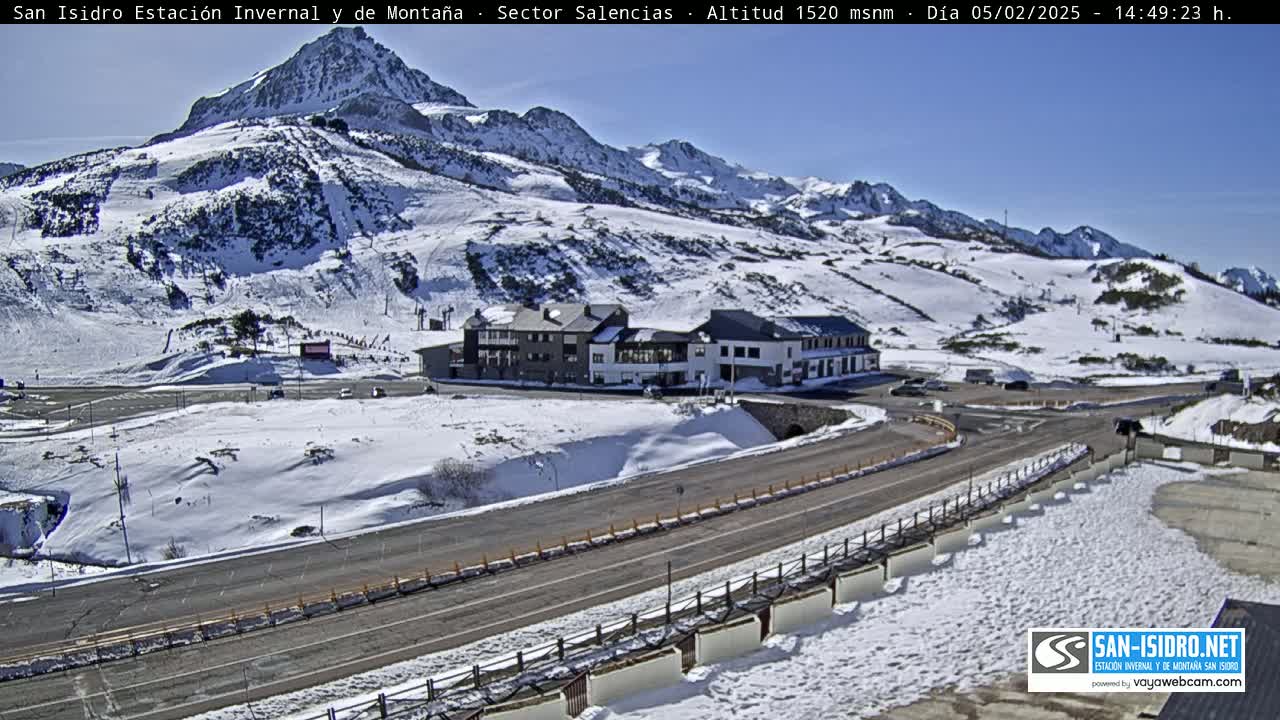 A snow-covered mountain landscape with a building complex and a road curving through the scene under a clear blue sky.