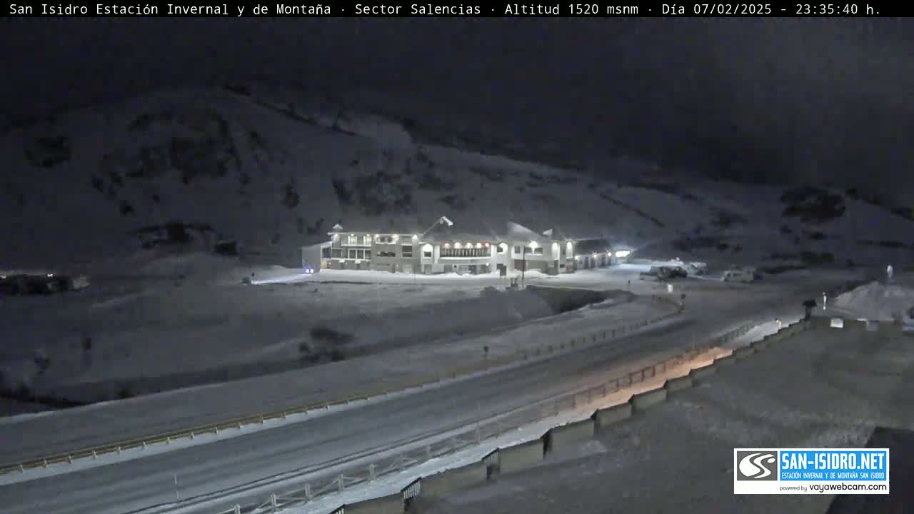A snow-covered landscape at night, featuring a lit building near a road.