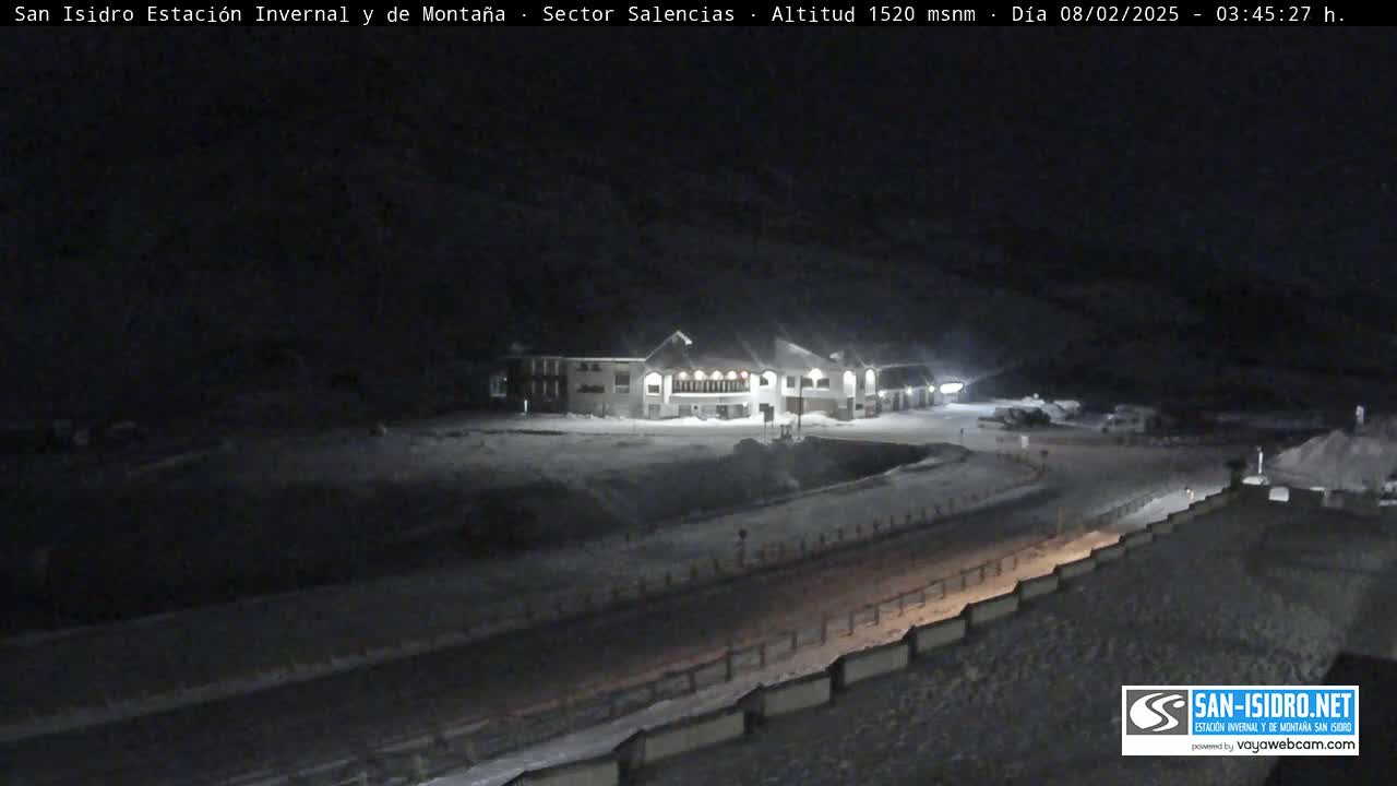 A snow-covered landscape at night, featuring a building and a road, under dark, possibly cloudy skies.
