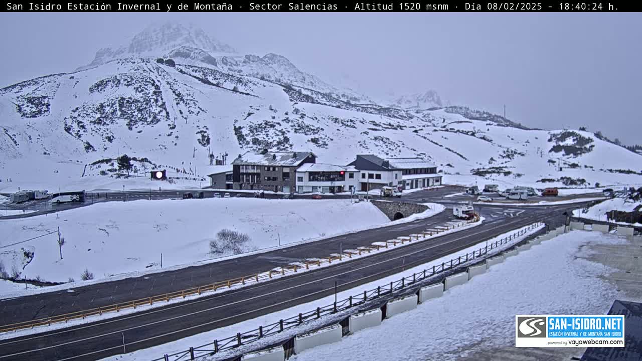 A snow-covered mountainside with ski runs, a road, and several buildings is visible under an overcast sky.