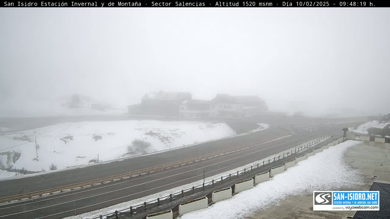 A snow-covered landscape with a road and buildings is shrouded in heavy fog.